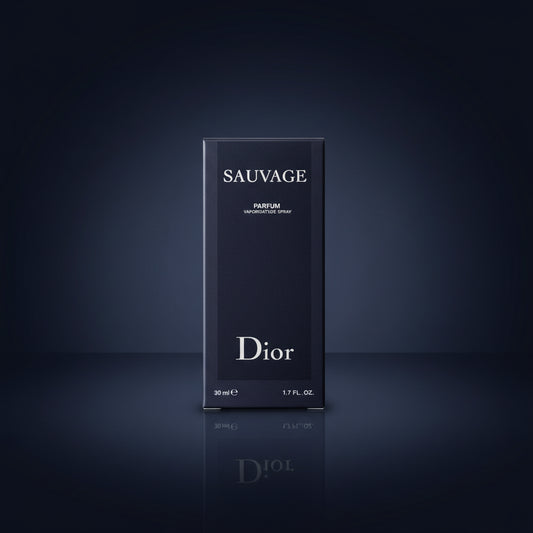 A hand holds a Dior Sauvage Parfum 10ml travel pack box in front of several matching Dior boxes, with a Cartier poster in the background.