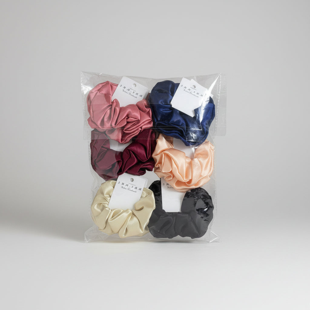 Six satin hair scrunchies in assorted colors, packaged in a clear plastic bag with white paper tags, placed on a wooden surface.